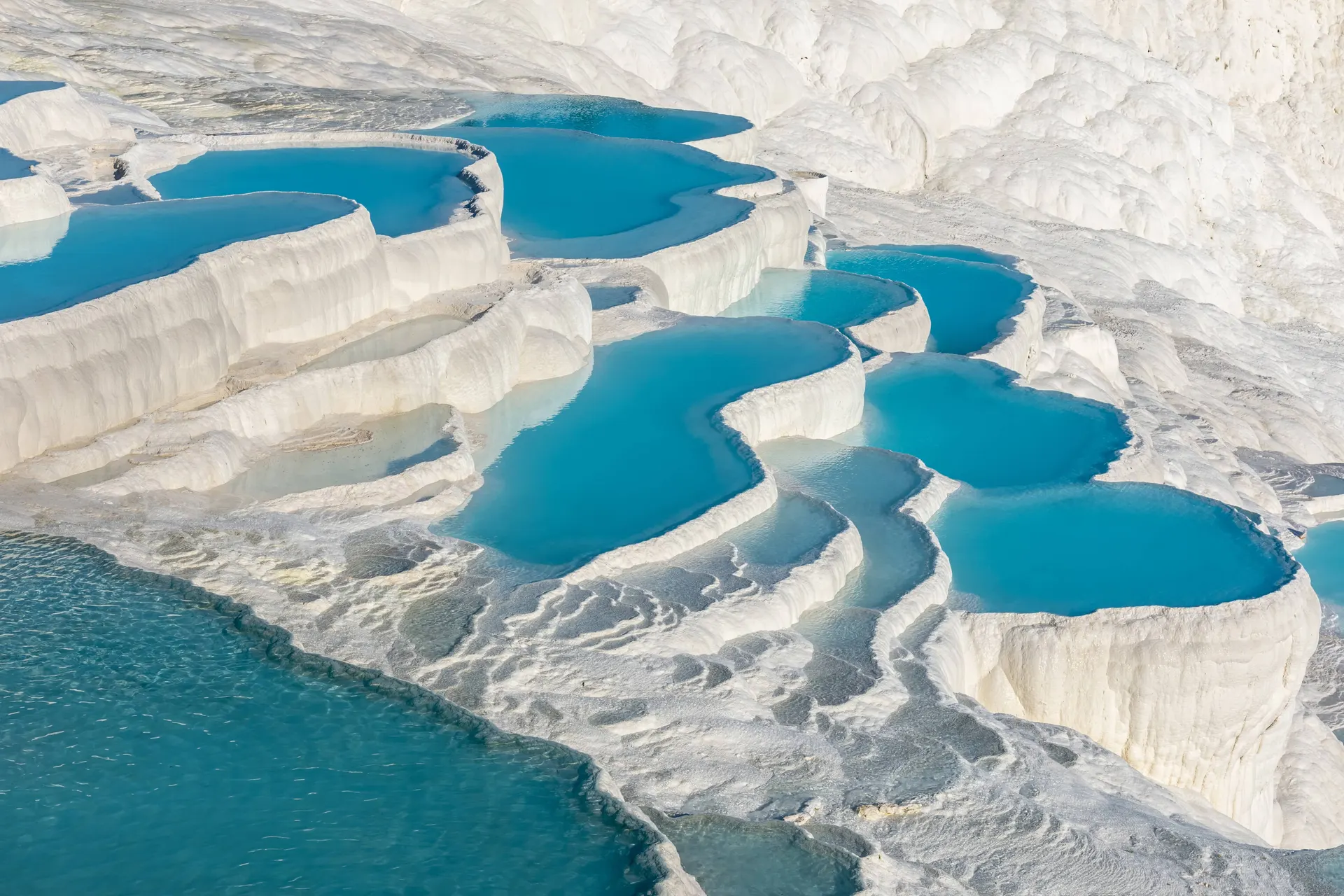 Turquoise thermal pools among the white travertine terraces of Pamukkale, Türkiye