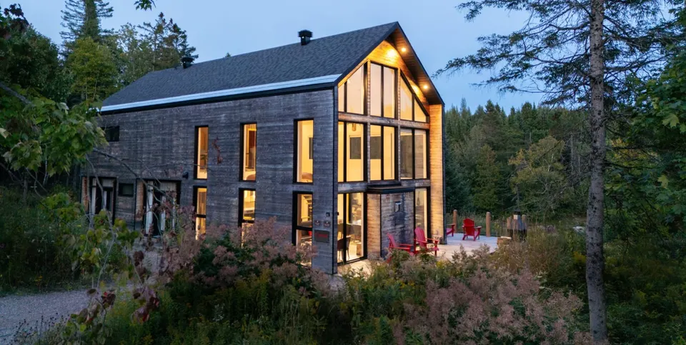 Le Baluchon's illuminated timber Canoer's Chalet surrounded by Quebec forest at dusk